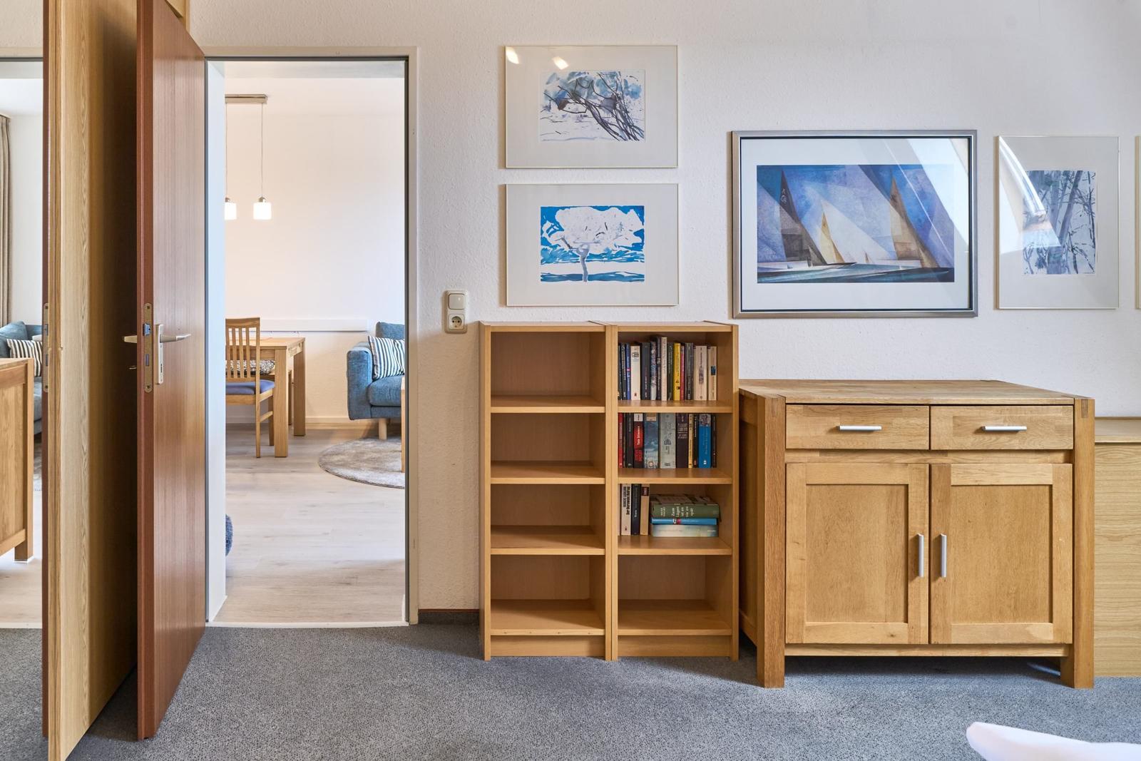 Eingangsbereich mit Bücherregal und Schrank. Durchgang in Wohnzimmer mit Tisch und Sofa.
