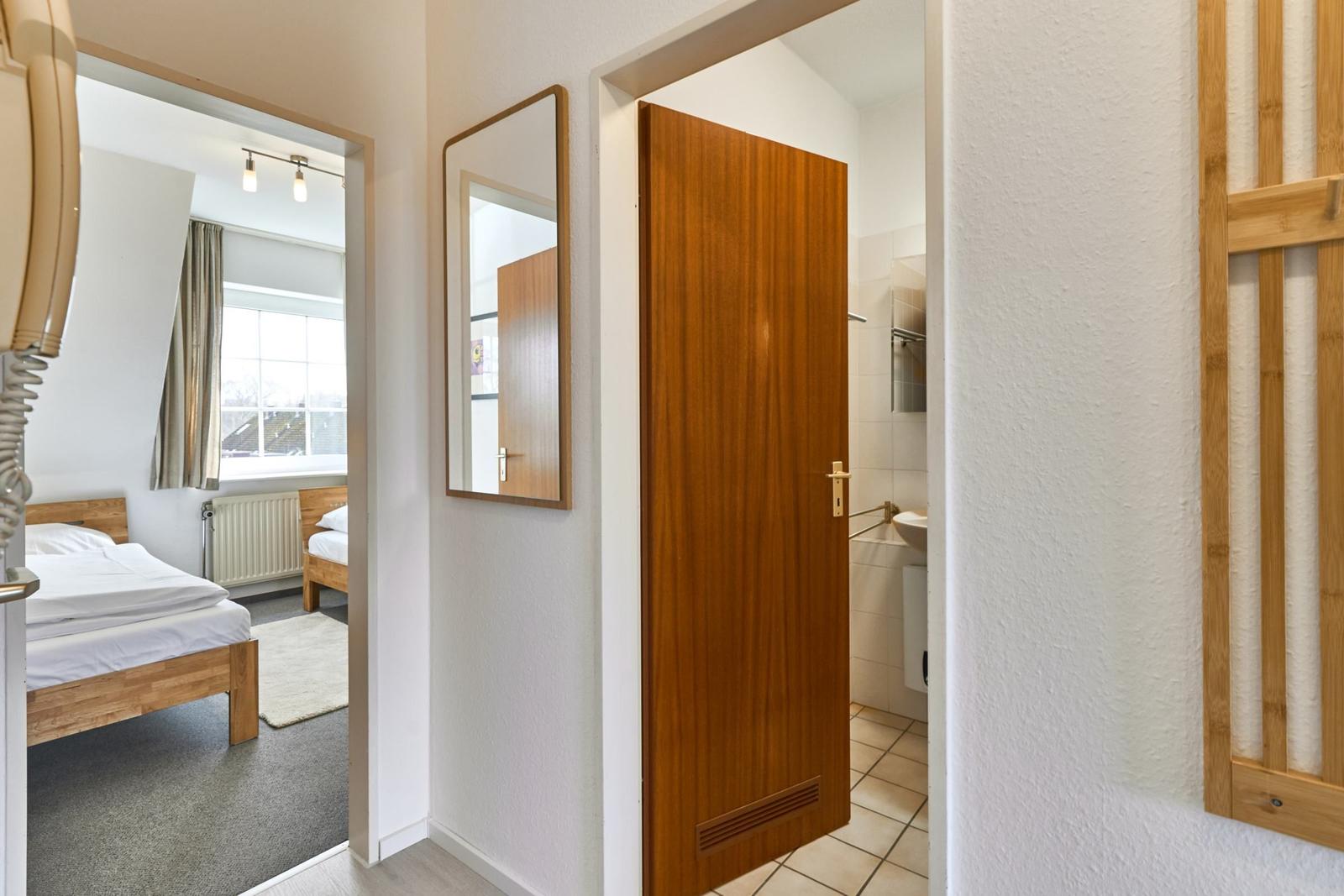 Schlafzimmer mit Bett und Fenster. Tür führt in Bad mit Waschbecken.