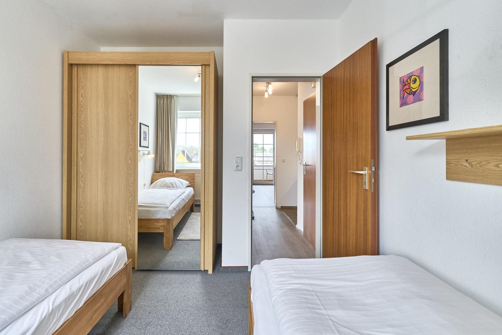 Zwei Schlafzimmer mit Betten und Holztüren. Blick in Flur und weiteres Zimmer.