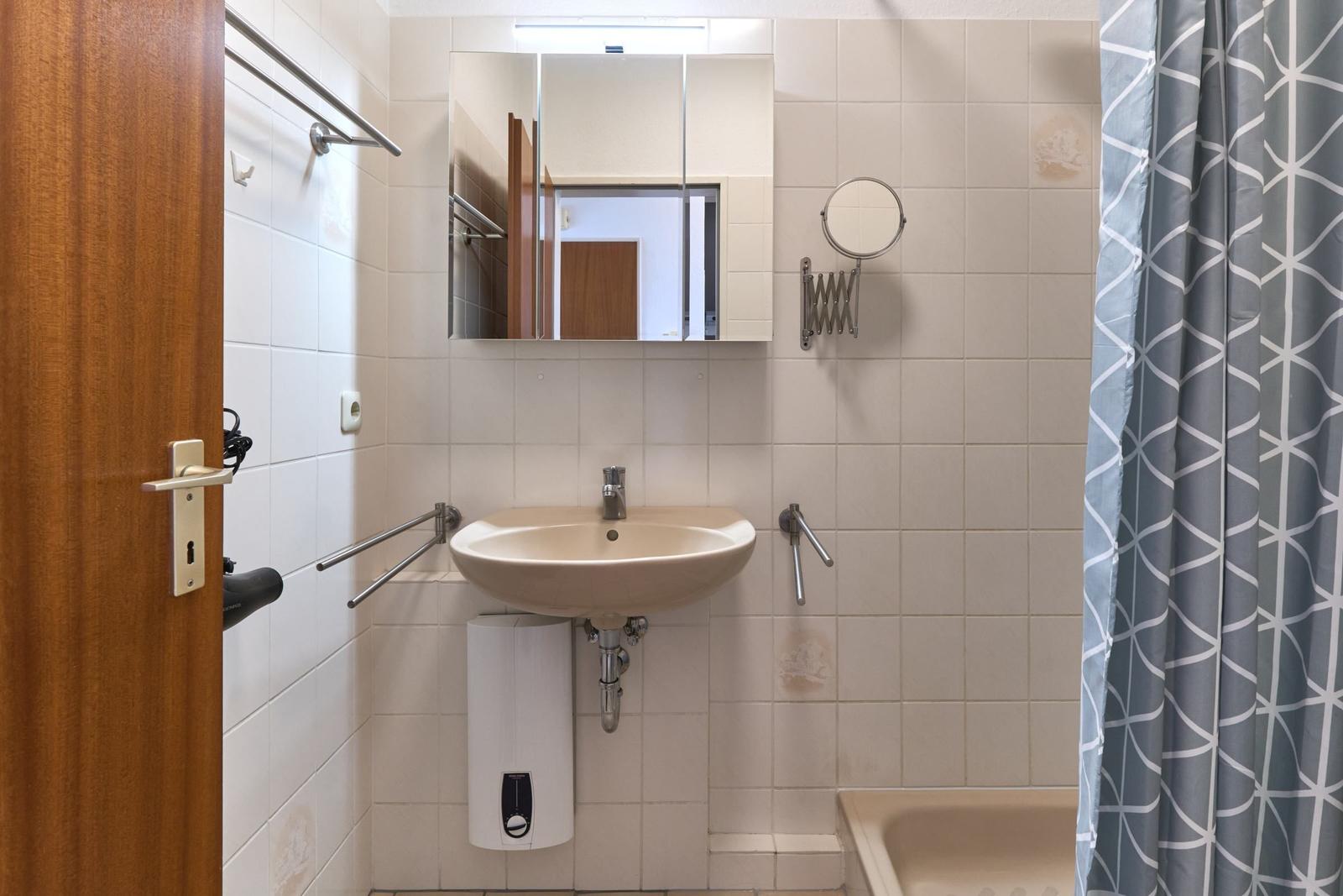 Badezimmer mit Waschbecken, Spiegel, Duschvorhang und Heizkörper.