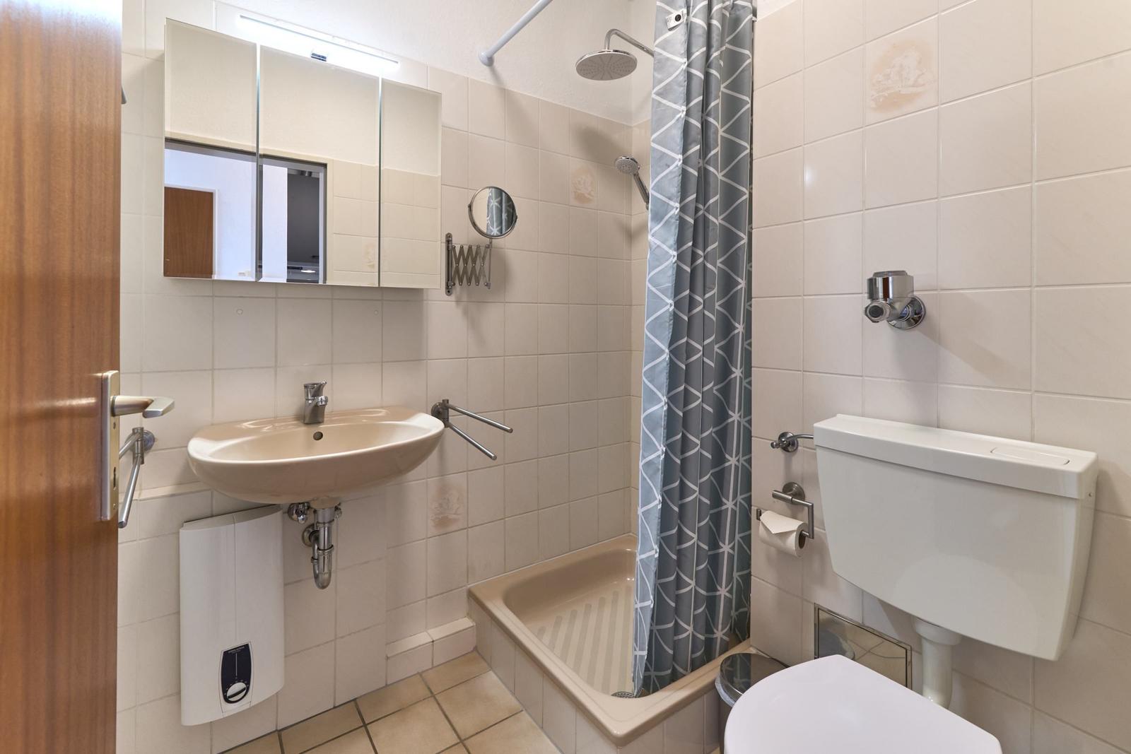Badezimmer mit Dusche, Waschbecken und Toilette. Fliesenwand und graue Duschvorhang.