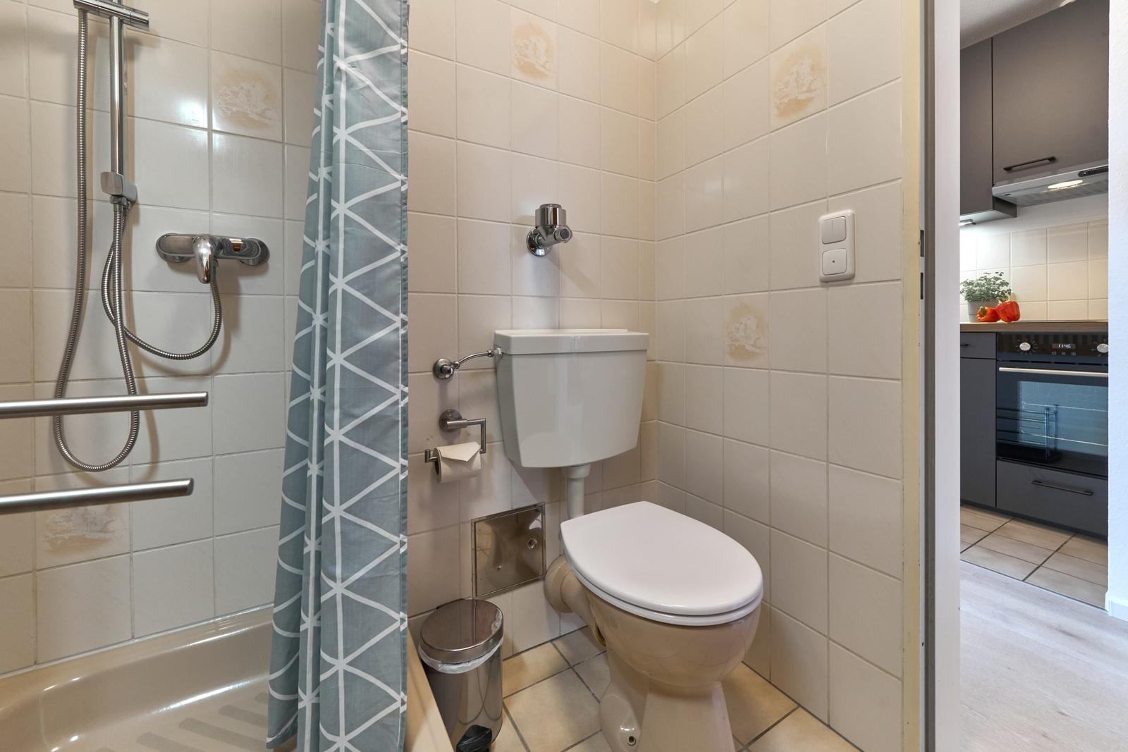 Bad mit Dusche, Toilette und grauem Vorhang.