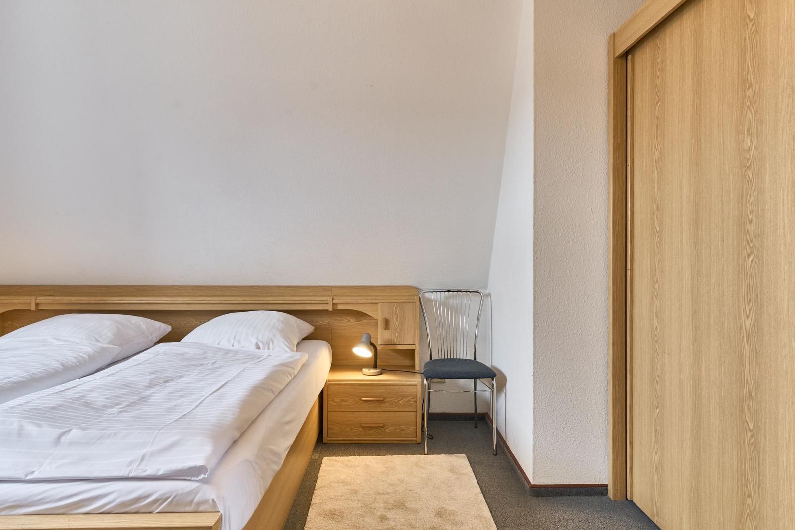Schlafzimmer mit Bett, Nachttisch und Stuhl. Holzmöbel und Kleidungsschrank.
