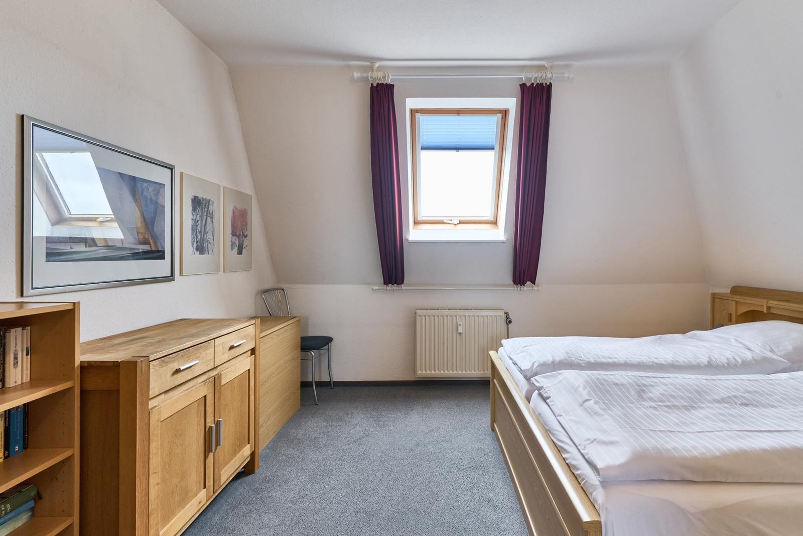 Schlafzimmer mit Doppelbett, Holzmöbeln und Fenster mit Vorhängen.