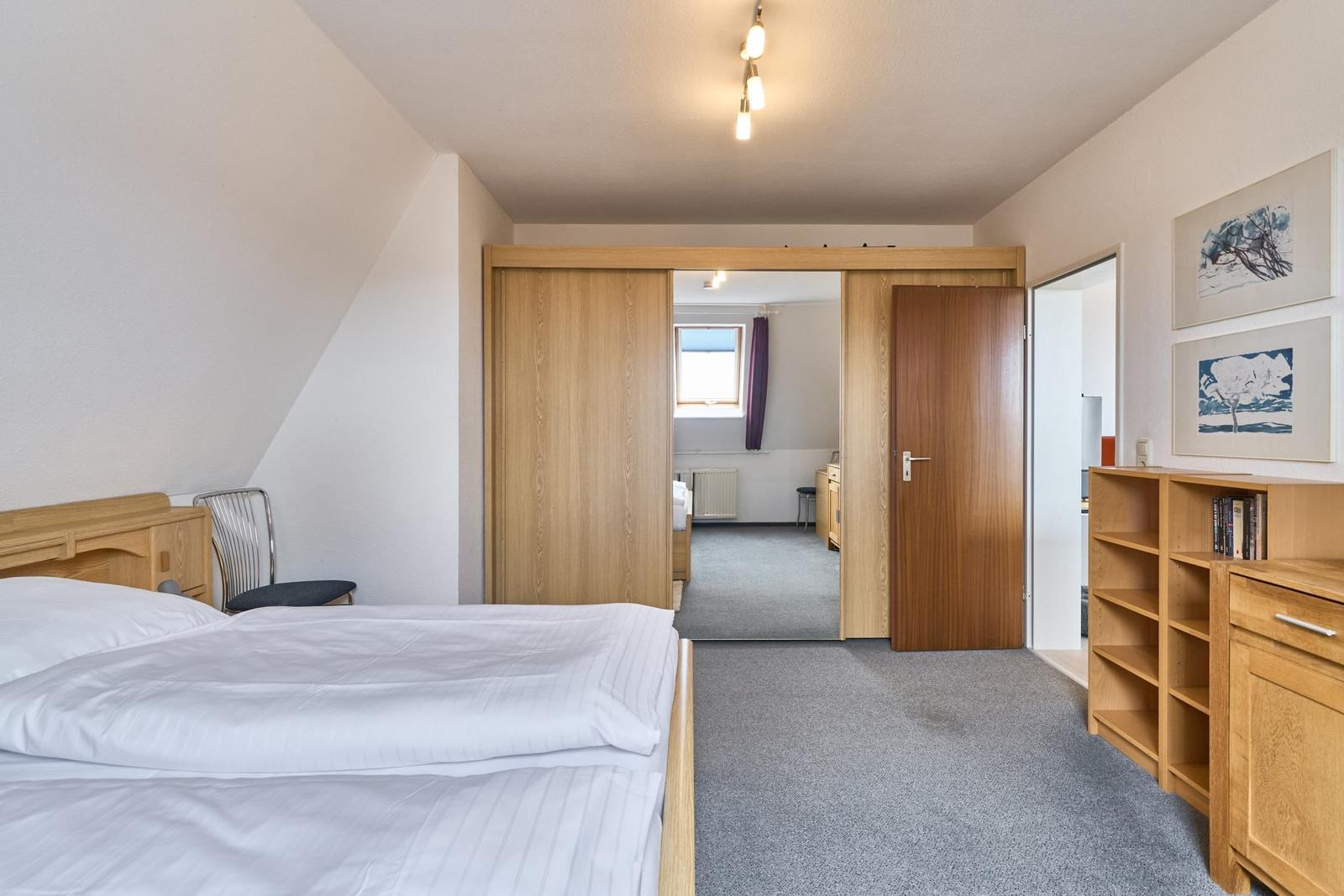 Schlafzimmer mit Bett, Schrank und Bücherregal. Durchgang zu weiteren Räumen.