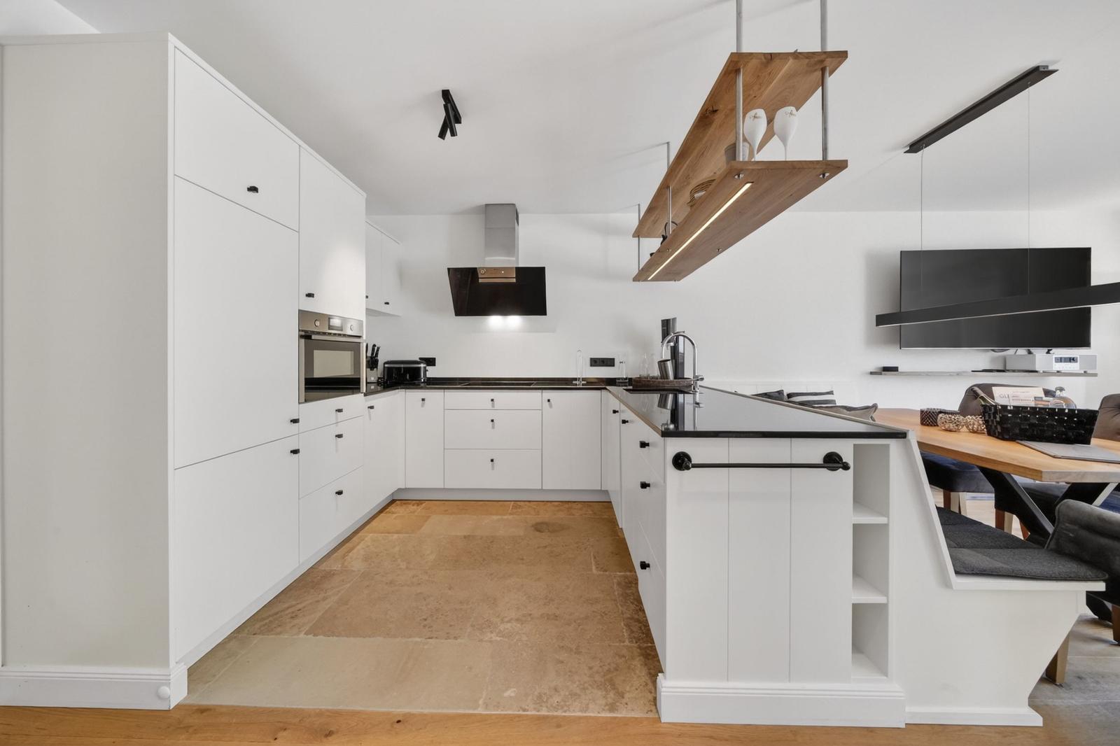 Moderne Küche mit weißen Schränken, Steinboden und Kücheninsel mit Sitzbank.