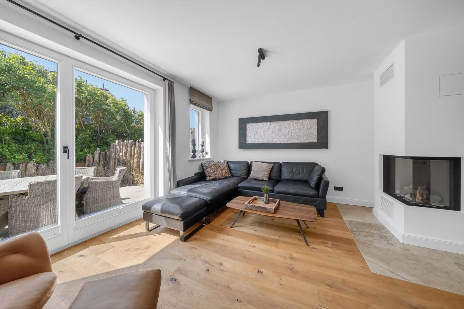 Wohnzimmer mit Ledersofa, Holzboden und Terrasse. Kamin und Wandbild sichtbar.