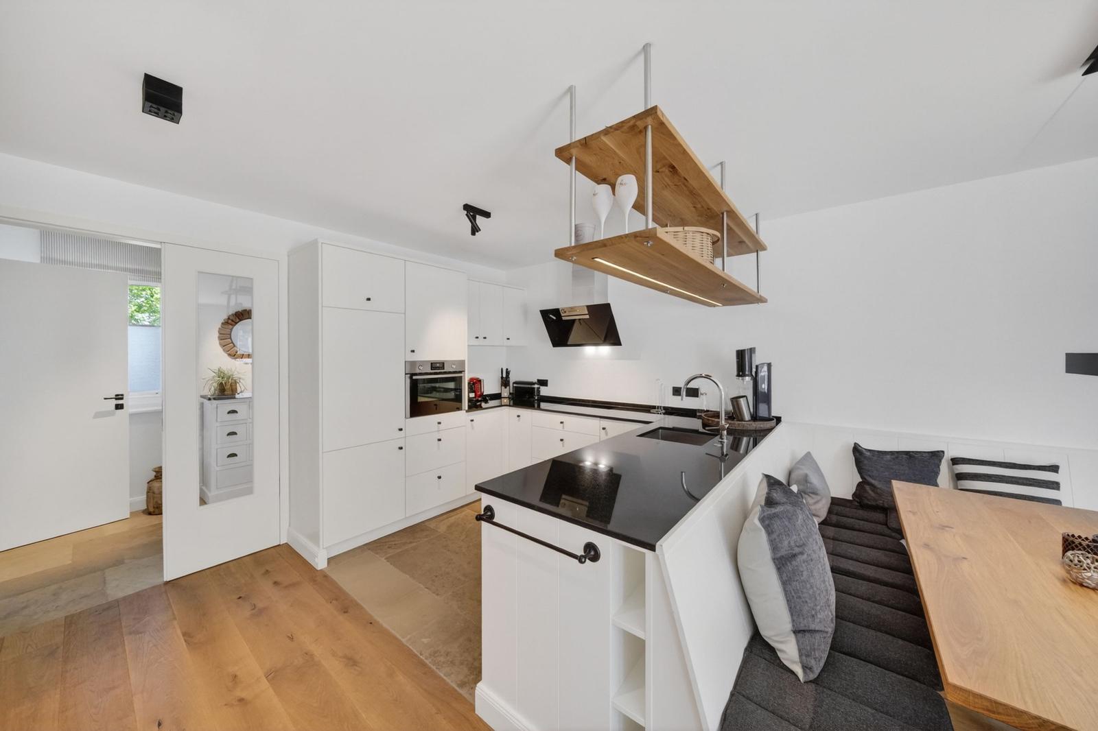 Küche mit Essbereich, weiße Schränke, schwarze Arbeitsplatte und Holzbank.