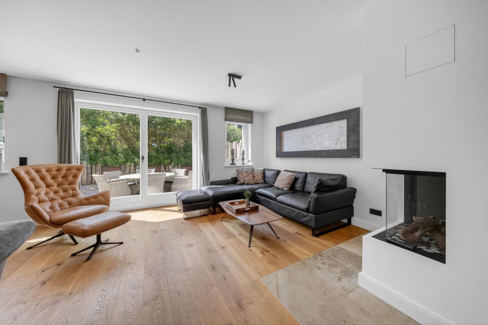 Wohnzimmer mit Ledersofa, brauner Ledersessel und Holzboden. Durchgangstür zum Garten.