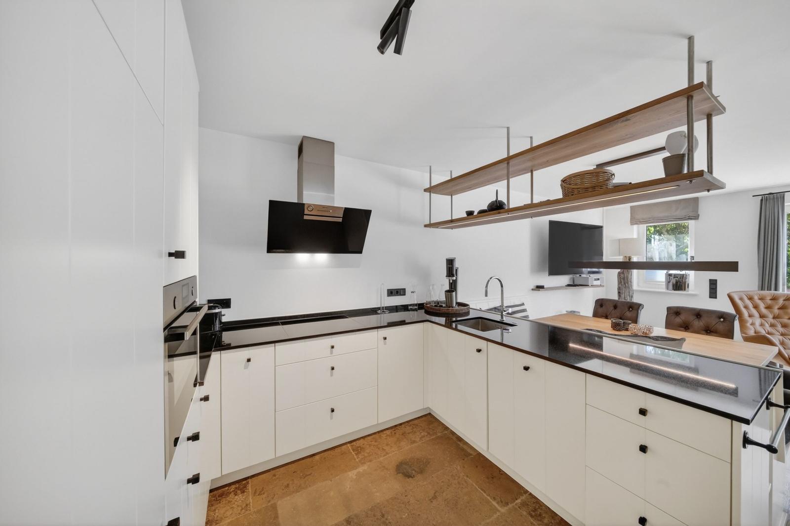 Moderne Küche mit weißen Schränken, schwarzer Arbeitsplatte und Holzregalen.