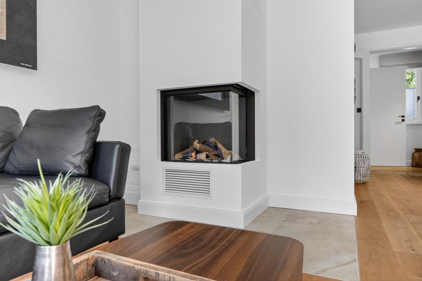 Ein Wohnzimmer mit einem modernen Kamin, einem schwarzen Sofa und einem Holztisch.