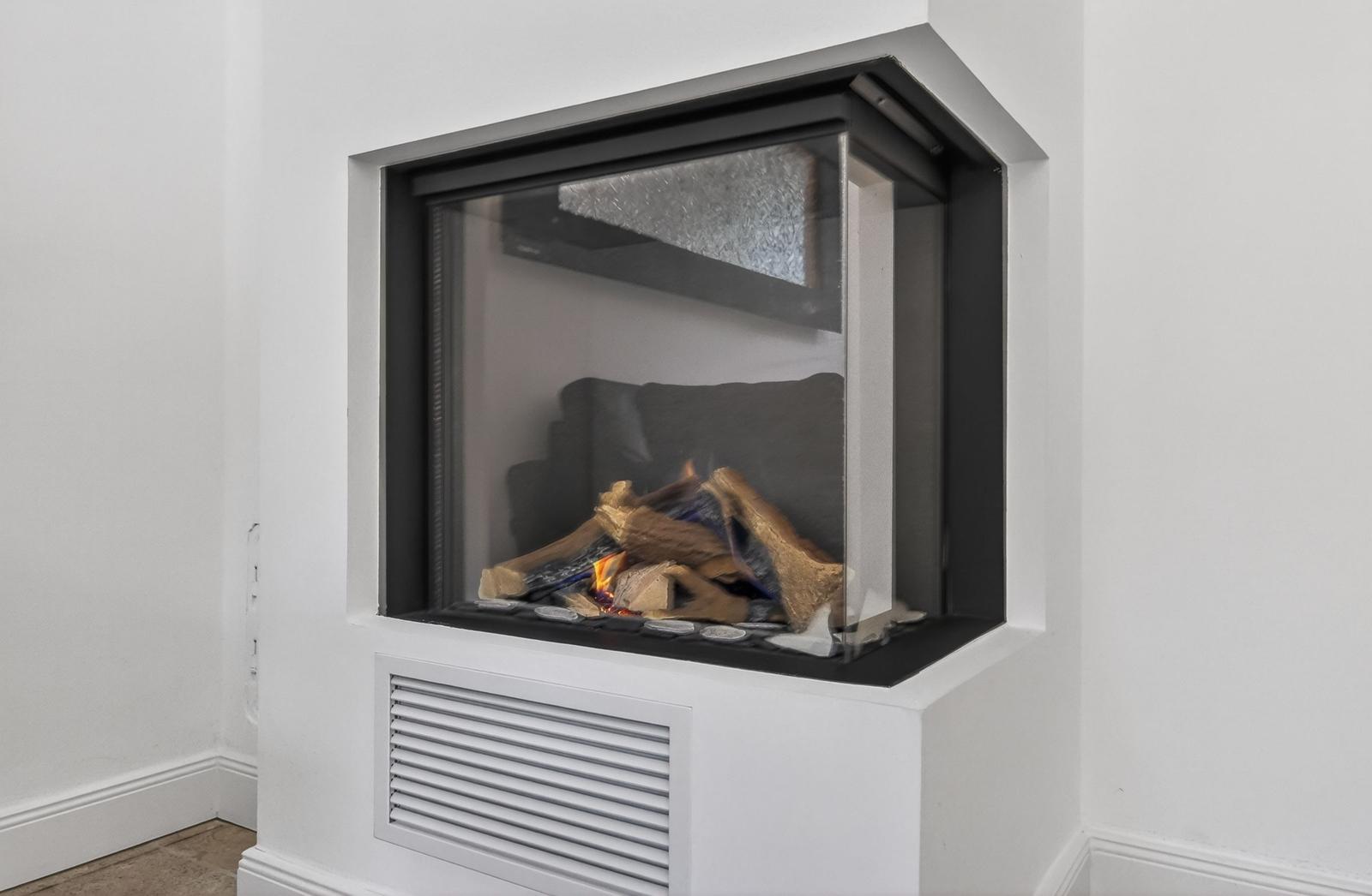 Ein moderner Kamin mit brennenden Holzscheiten in einem weißen Wandrahmen.