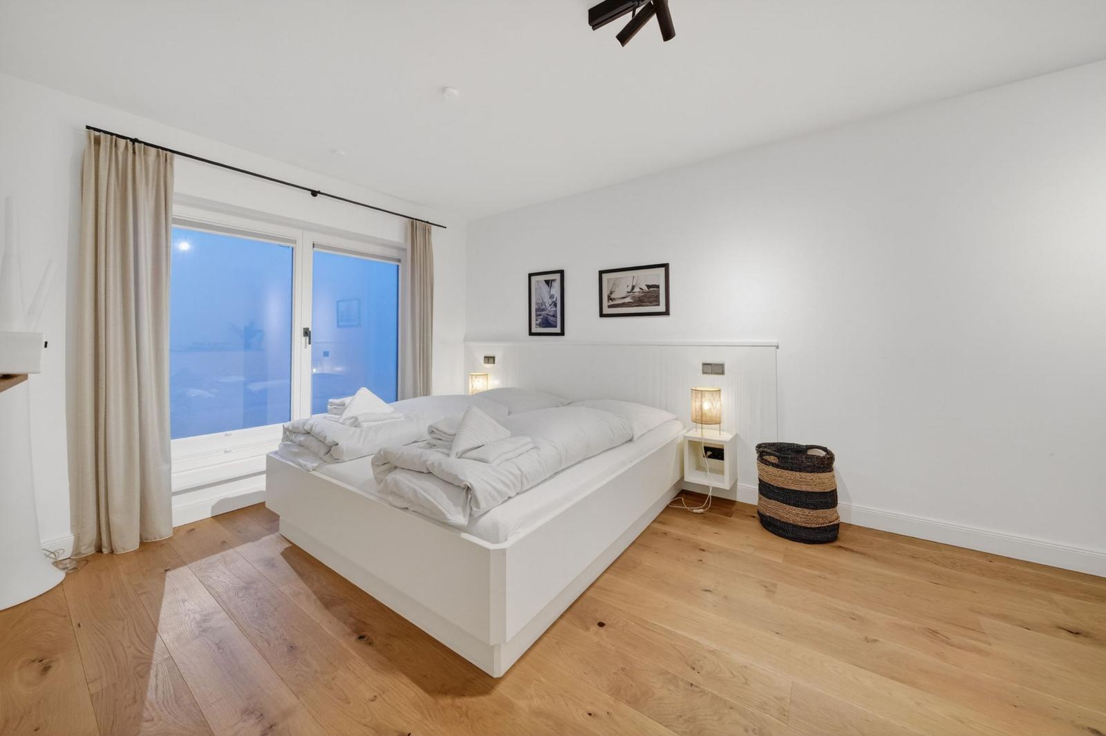 Schlafzimmer mit weißem Bett, Holzboden und Fenster mit Blick.