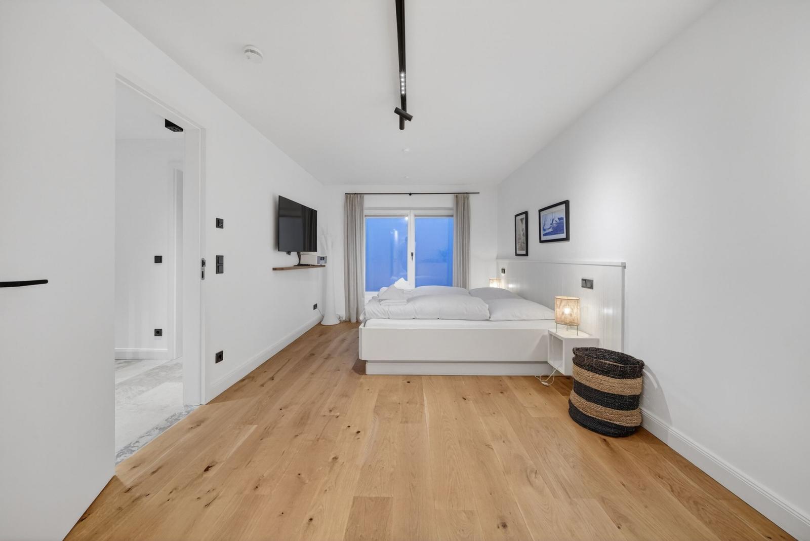 Schlafzimmer mit Holzboden, Bett, Fernseher und Fenster zur Aussicht.