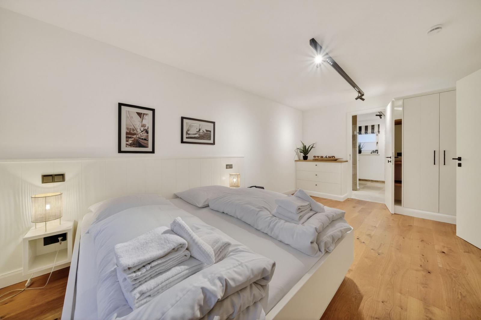 Schlafzimmer mit Doppelbett, Holzboden und Kleiderschrank. An der Wand hängen zwei Bilder.