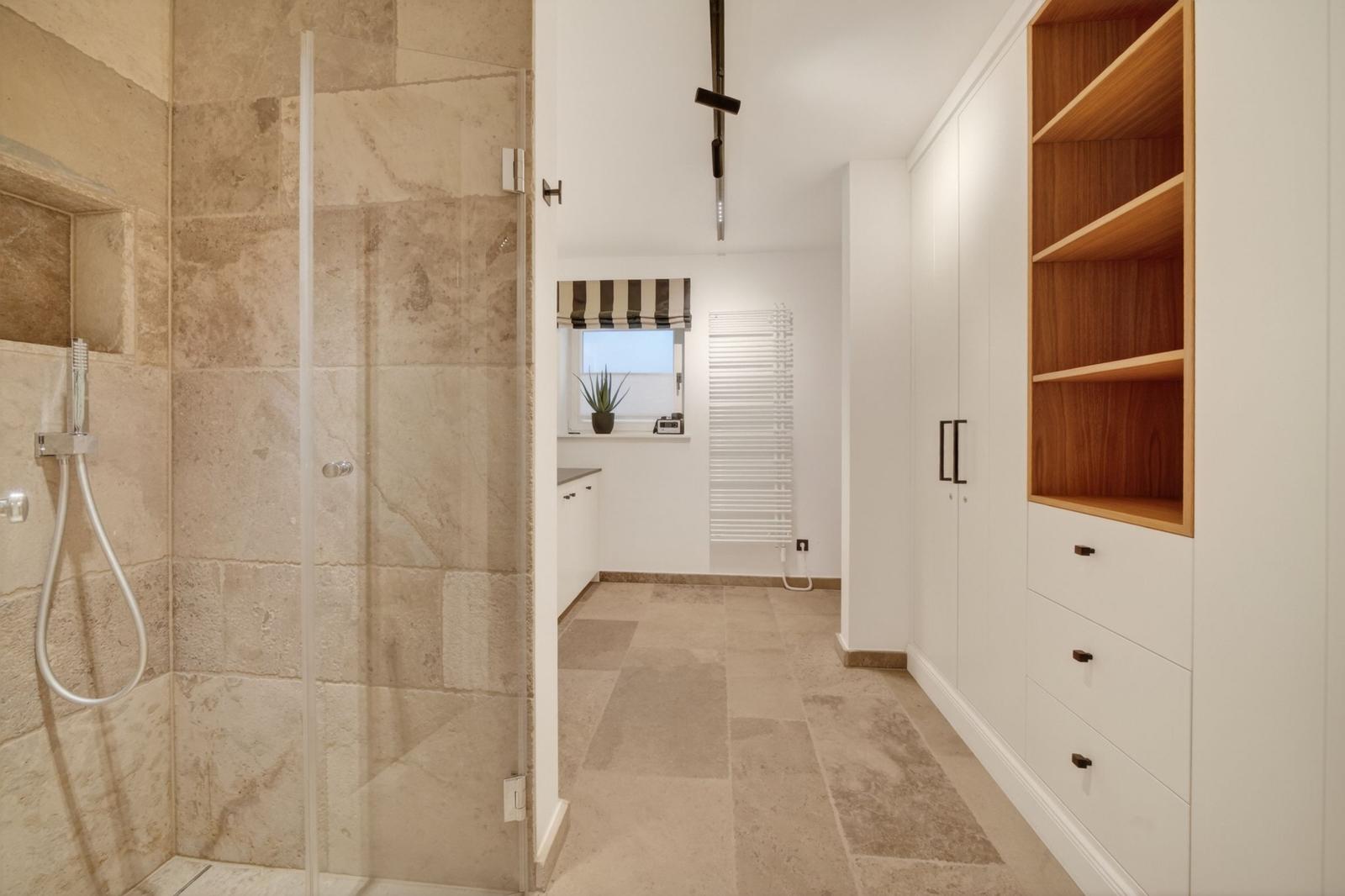 Dusche mit Glaswand, Kleiderschrank und Fenster mit Rollladen.
