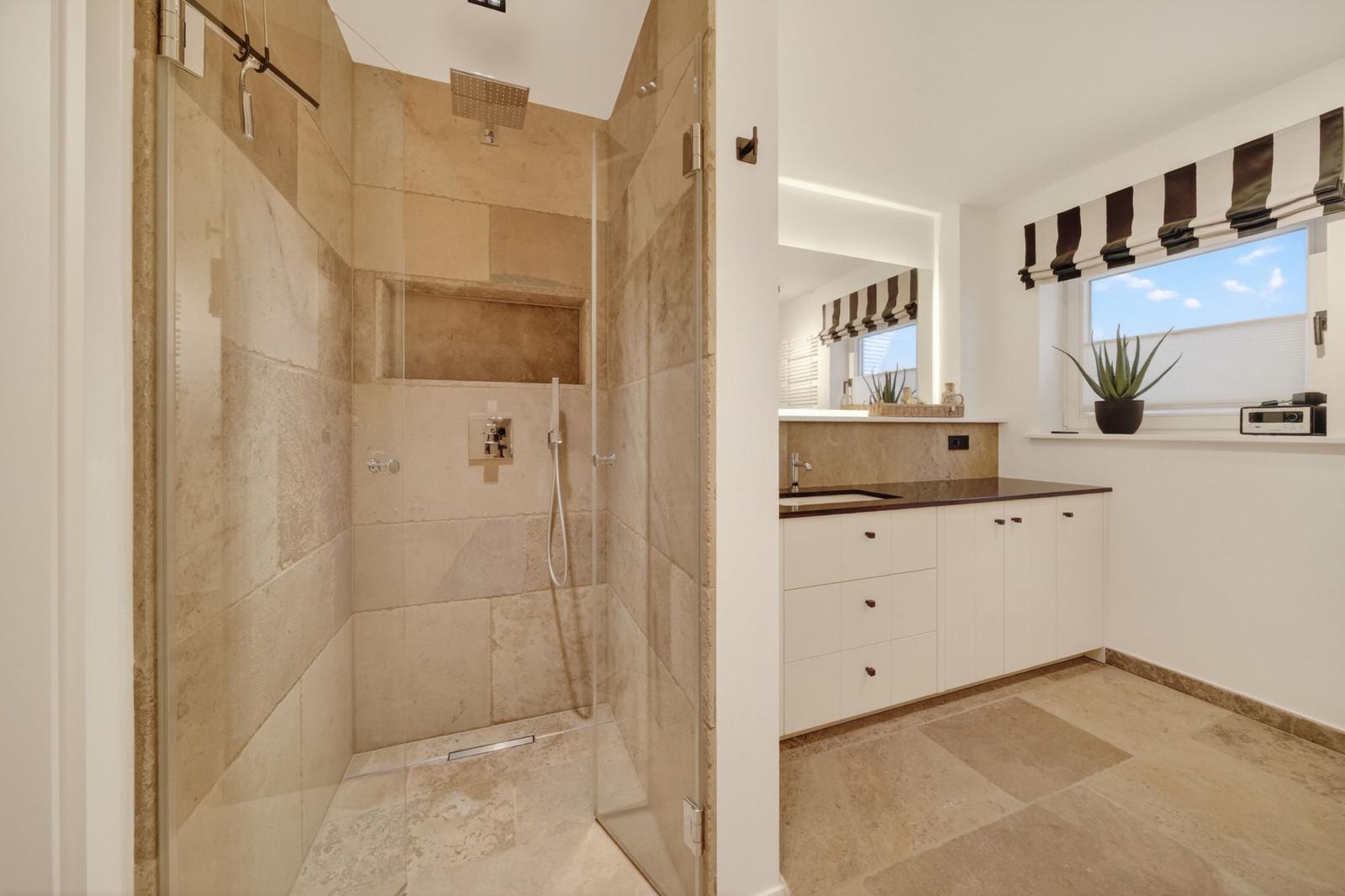 Dusche mit Glaswand, Waschbecken und Fenster mit Pflanze.