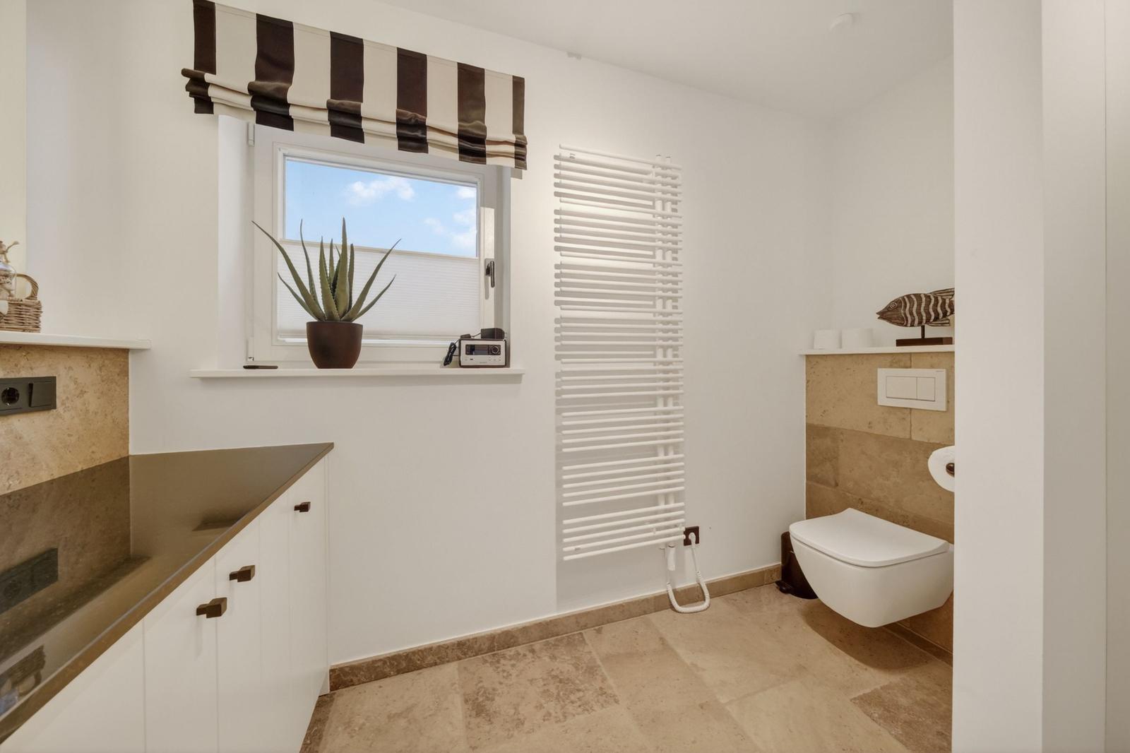 Badezimmer mit Fenster, Pflanze, Heizkörper und Wandtoilette.