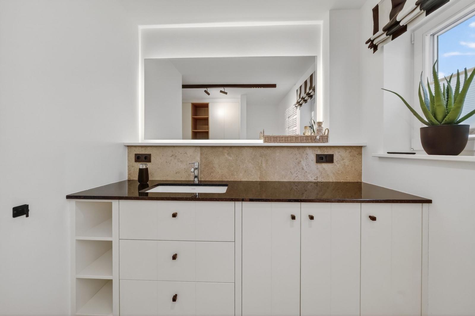 Waschbecken mit Spiegelschrank und Pflanze auf Fensterbank.