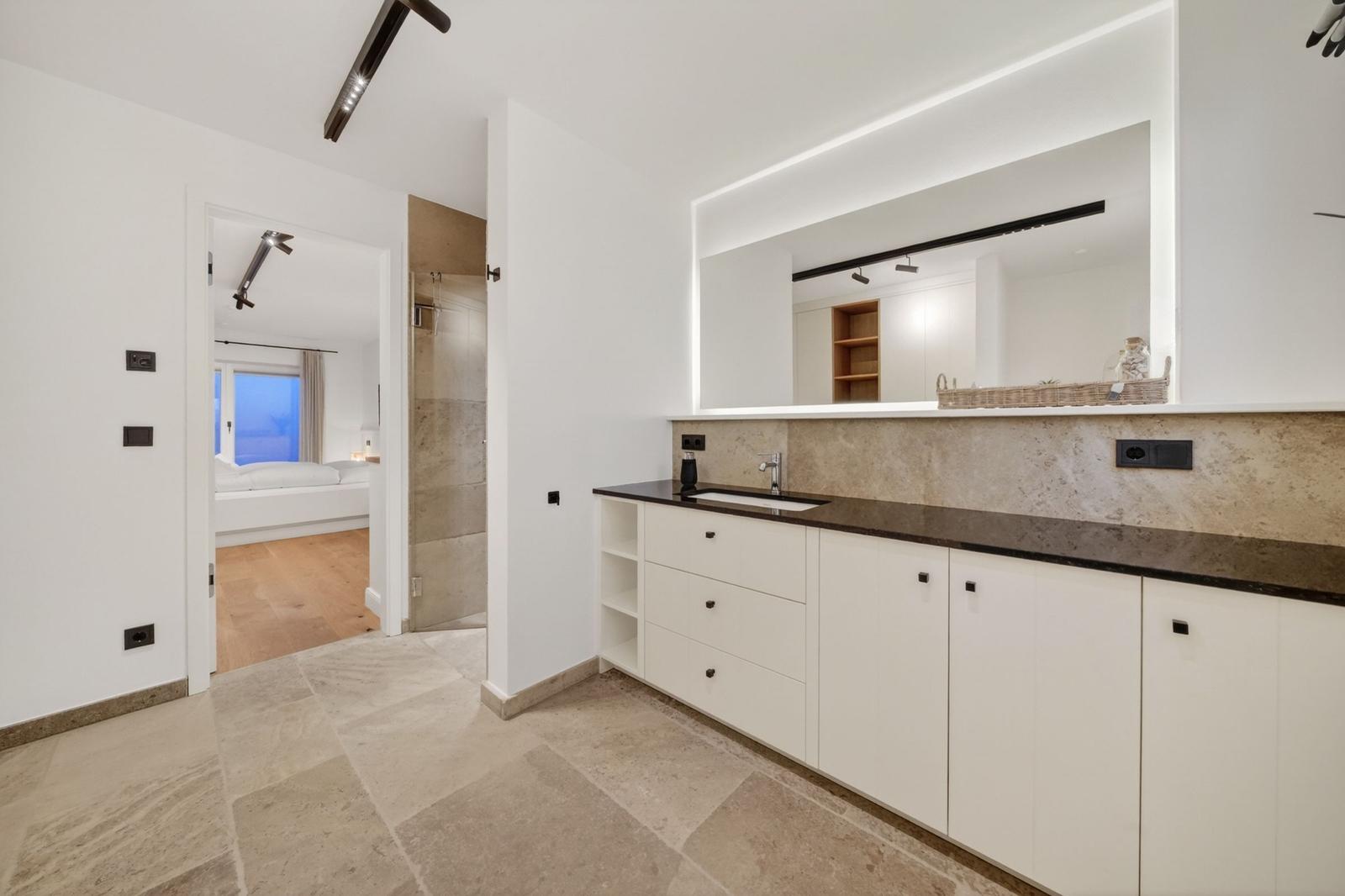 Badezimmer mit Waschtisch, Spiegel und Blick in Schlafzimmer und Dusche.