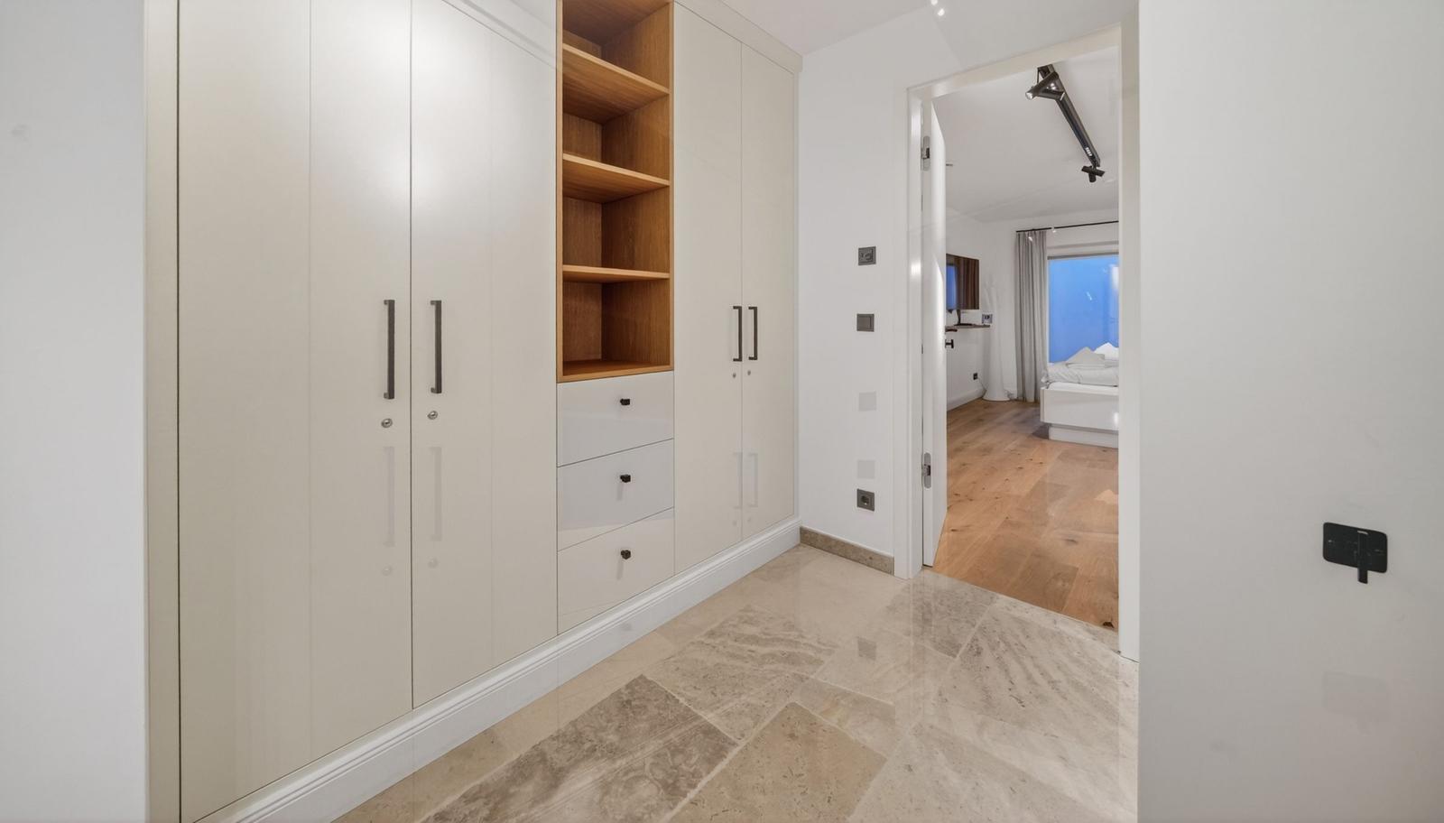 Großer Kleiderschrank mit Holzregalen und Schubladen. Blick in das Schlafzimmer mit Holzboden.