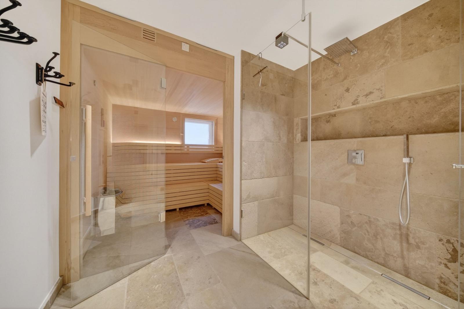 Dusche mit Glaswand und Sauna im Hintergrund.