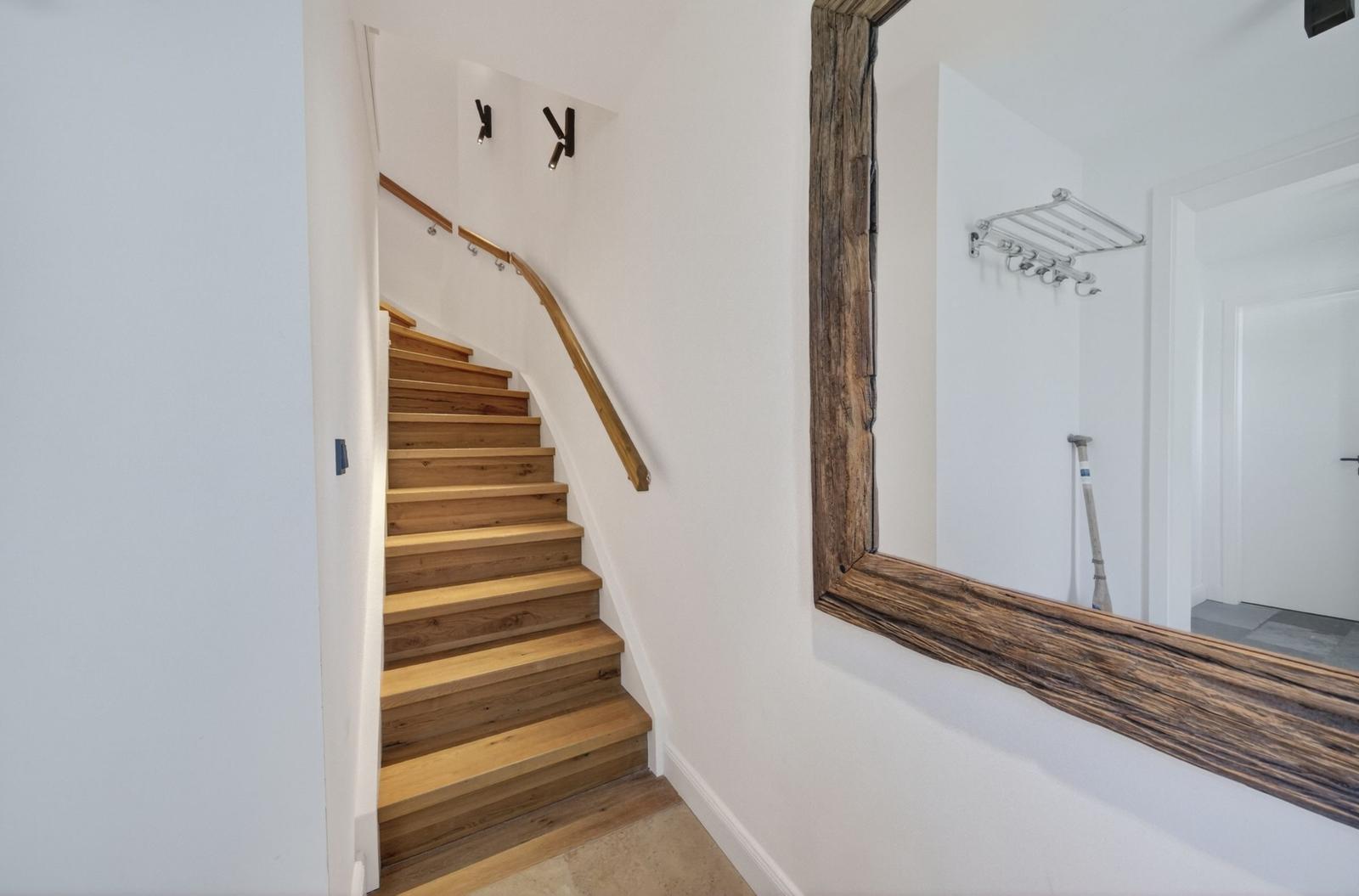 Holzgetreppe mit Geländer führt nach oben. Großer Spiegel mit rustikalem Rahmen an der Wand.