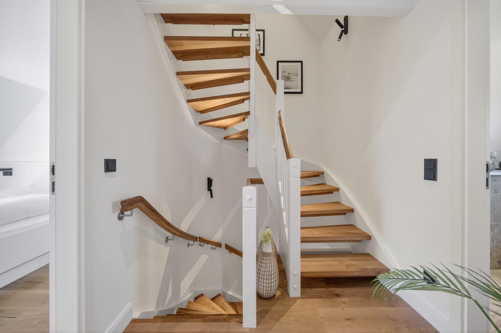 Holzgetreidete Treppe mit weißen Geländern und Wandbildern führt nach oben.