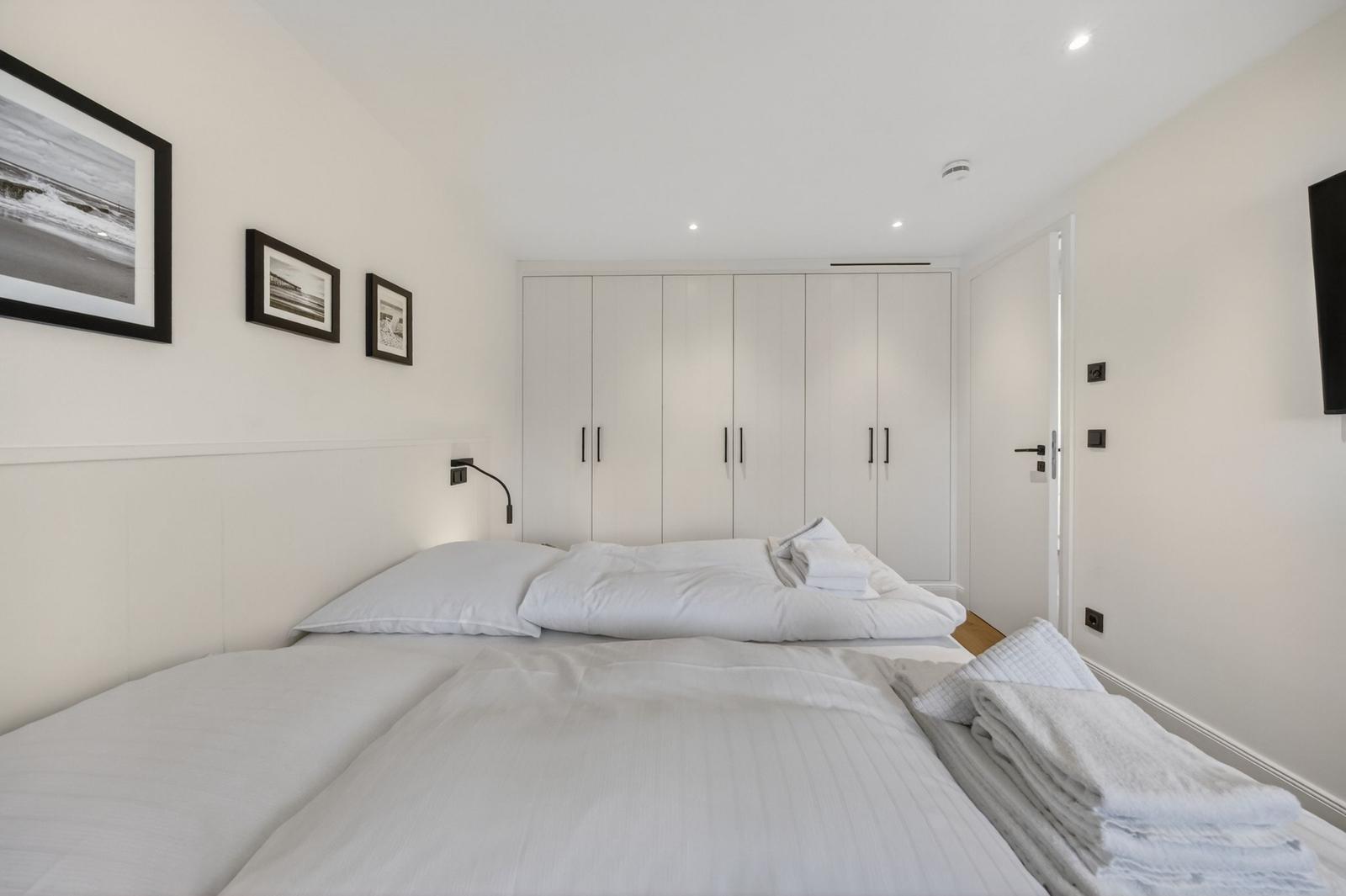 Schlafzimmer mit weißem Bett, Kleiderschrank und Wandbildern.