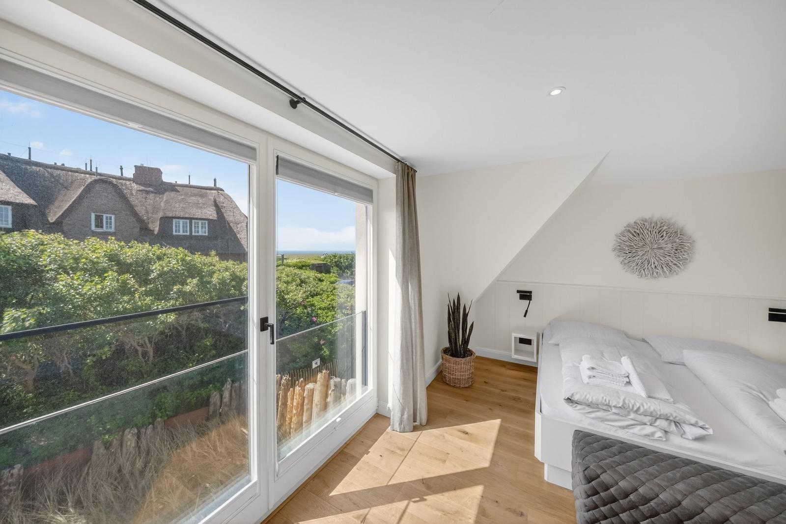 Schlafzimmer mit Balkon und Blick auf Dachhäuser und Meer.