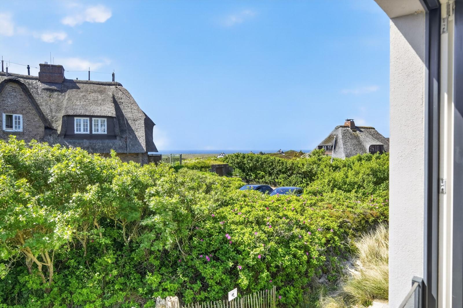 Von Balkon aus Blick auf traditionelle Häuser mit Strohdächern und grüne Büsche.