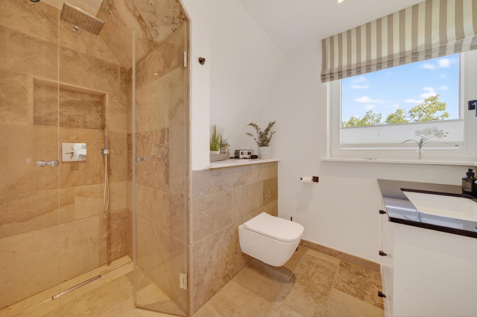 Bad mit Dusche, Toilette und Waschbecken unter Fenster mit Streifenrollo.