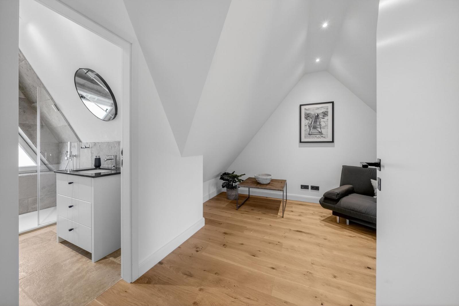 Schlafzimmer mit Dachschrägen, Holzboden und grauem Sofa. Neben dem Bad mit Duschbad.