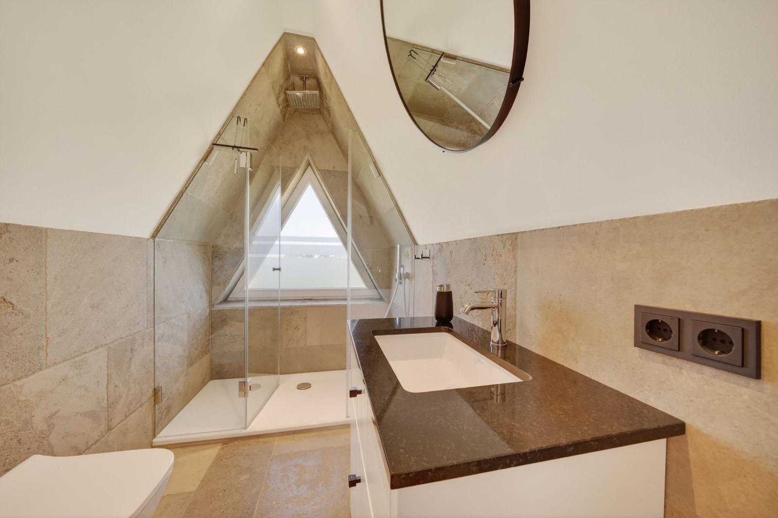 Badezimmer mit Dusche, Waschbecken und Toilette unter Dachschrägen.