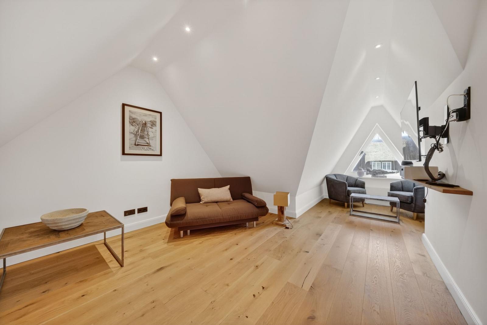 Ein Wohnzimmer mit Holzboden, braunem Sofa und zwei Sesseln unter einem Dach