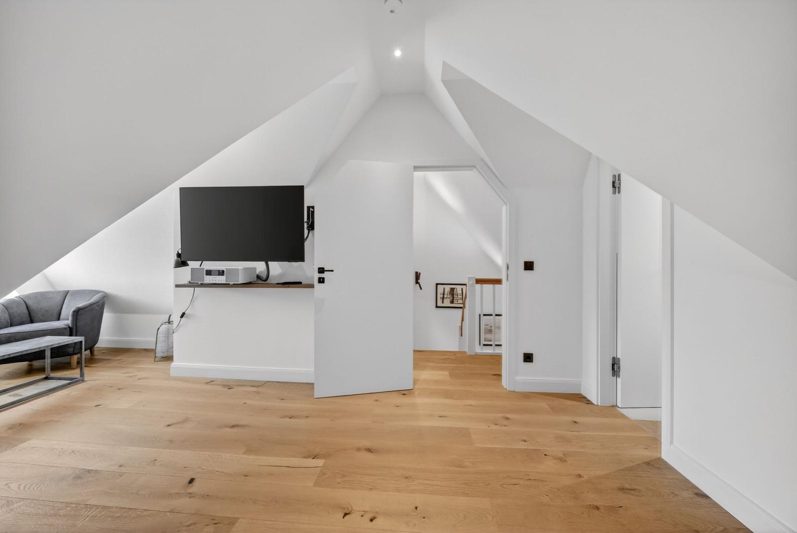 Wohnraum mit Fernseher, Sofa und Holzboden unter Dachschrägen.