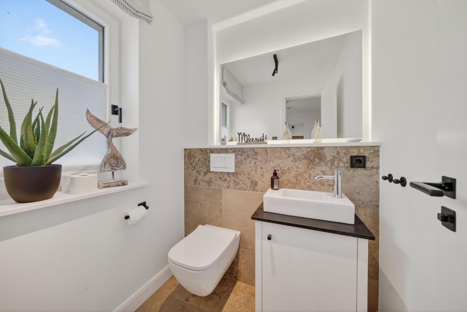 Badezimmer mit Waschbecken, Toilette und Fenster mit Pflanze.
