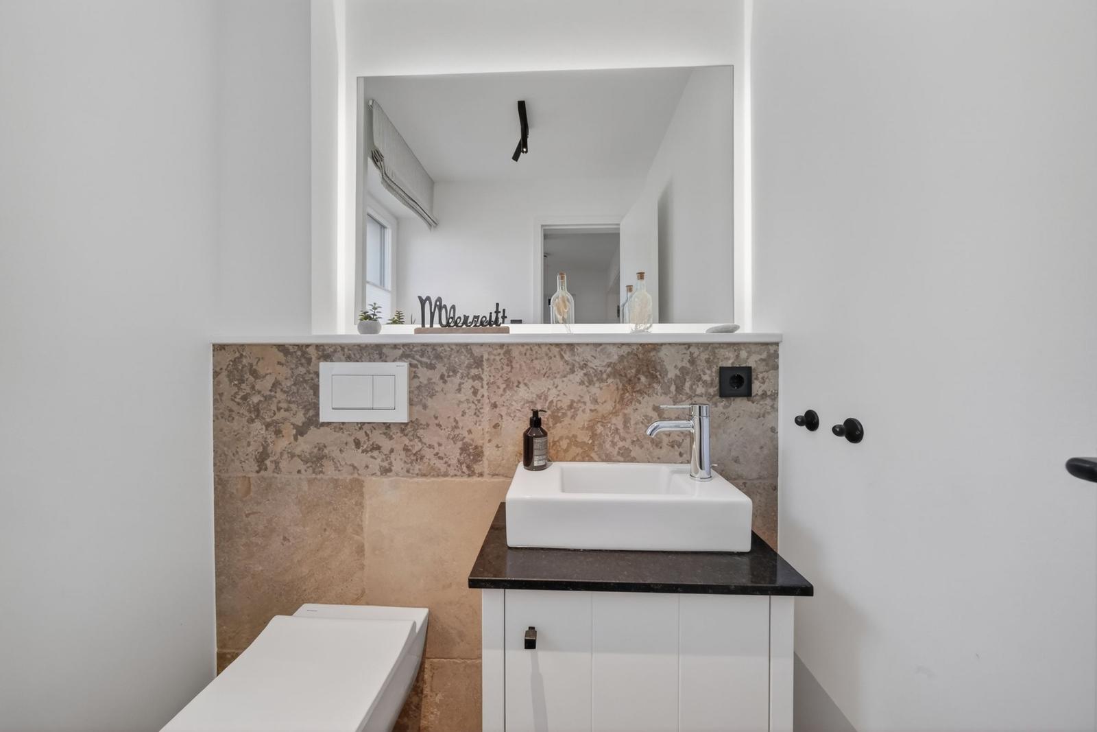 Bad mit Waschbecken, Spiegel und Toilette. Marmorwand und schwarze Arbeitsplatte.