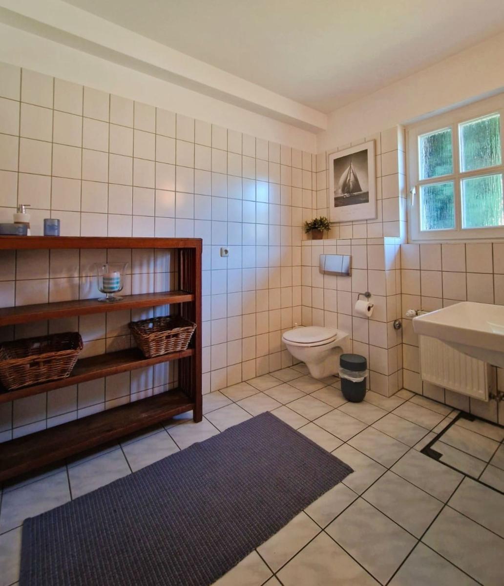 Badezimmer mit Toilette, Waschbecken und Holzregal. Fenster mit Blick nach draußen.