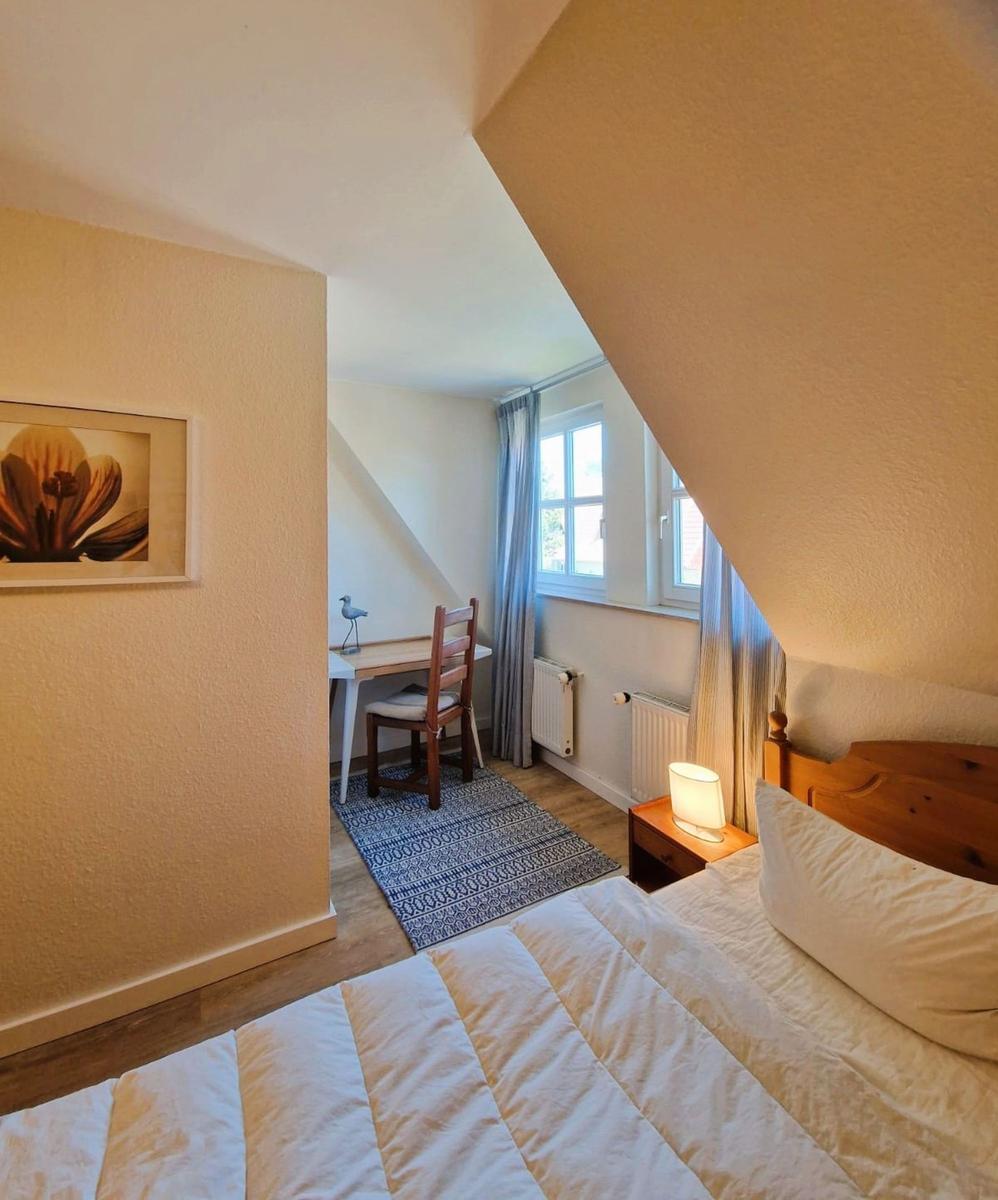 Schlafzimmer mit Bett, Nachttisch, Schreibtisch und Fenster.