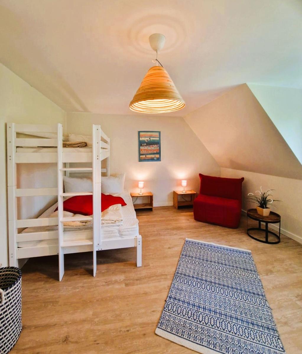 Ein Schlafzimmer mit Doppelstockbett, rotem Sessel und Holzboden.