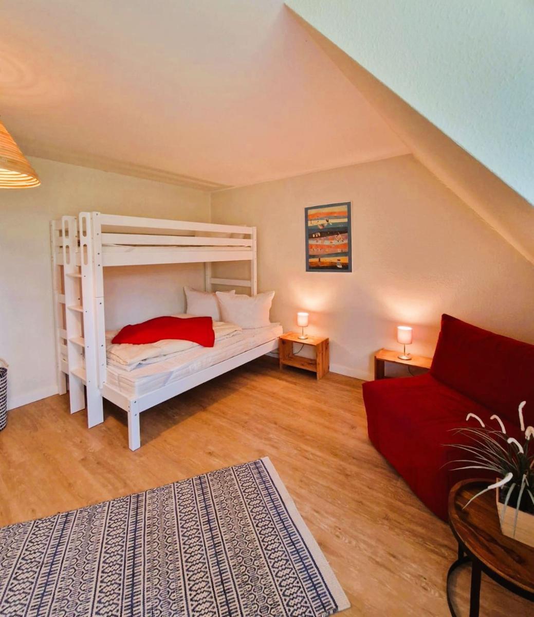 Zimmer mit Etagenbett, rotem Sofa und Holzboden. An den Wänden hängen Bilder.