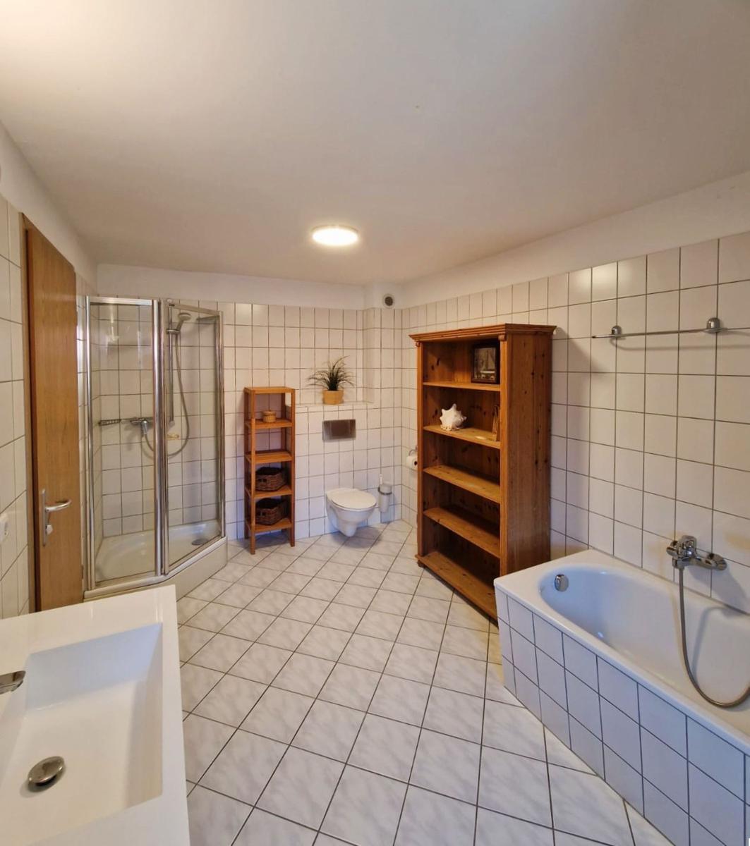 Badezimmer mit Dusche, Badewanne, Toilette und Holzregal.