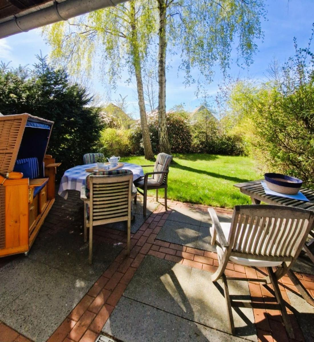 Terrasse mit Tisch, Stühlen und Liege unter Bäumen im Garten