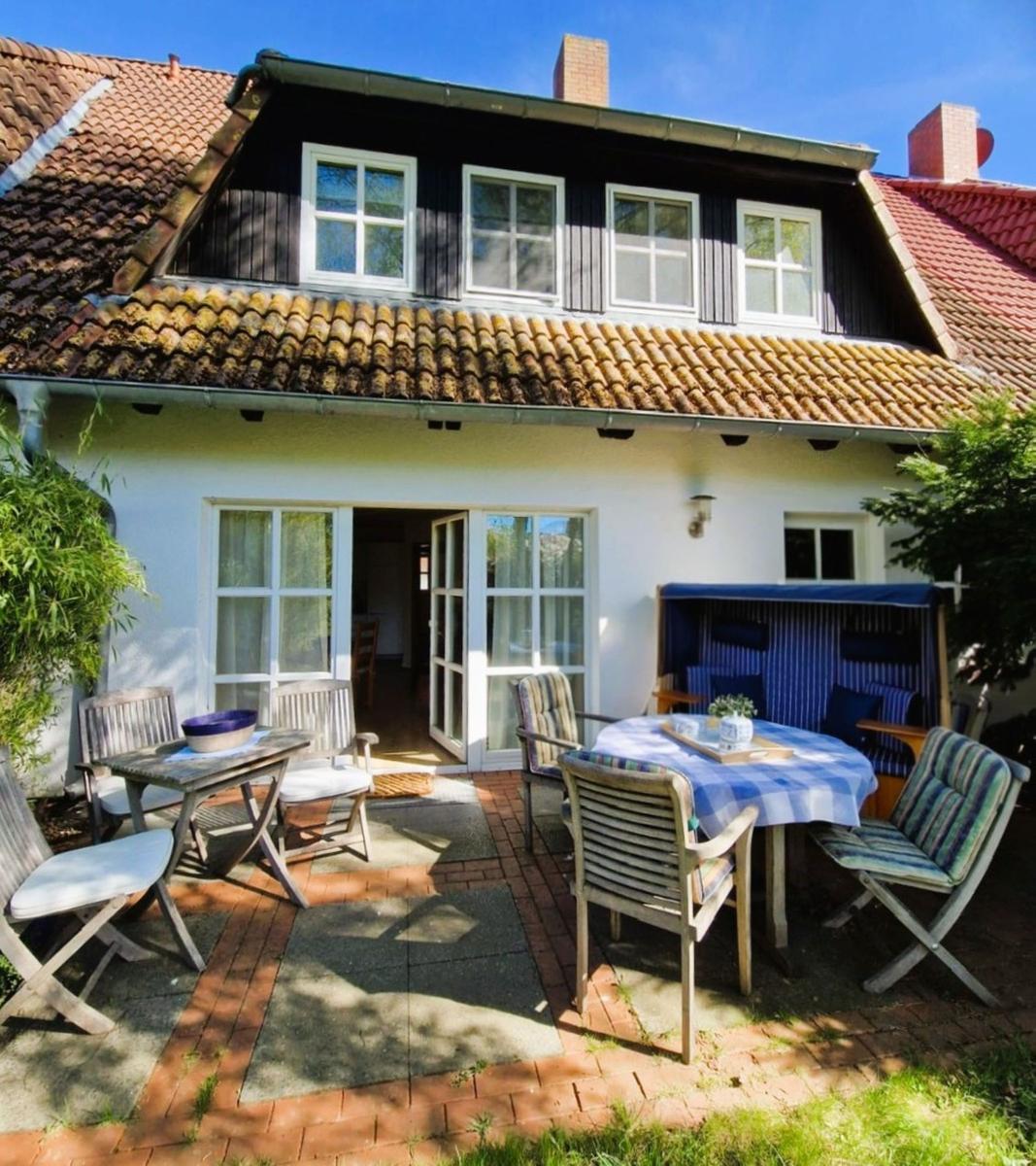 Haus mit Terrasse, Tisch, Stühlen und Strandkorb. Holzterrasse mit Garten.