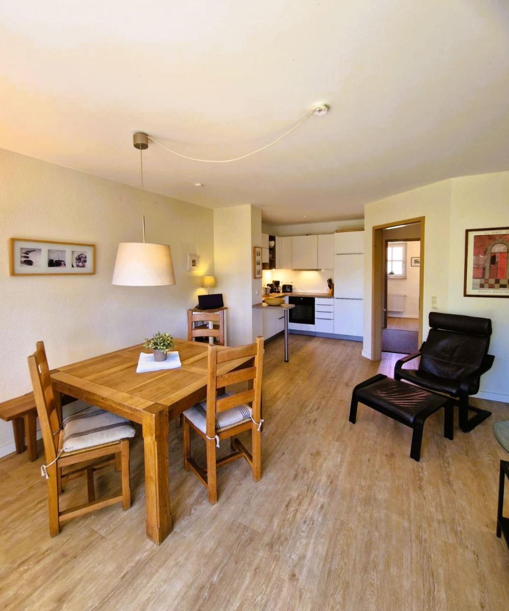 Esszimmer mit Holztisch und Stühlen, Küche im Hintergrund, schwarze Ledersessel