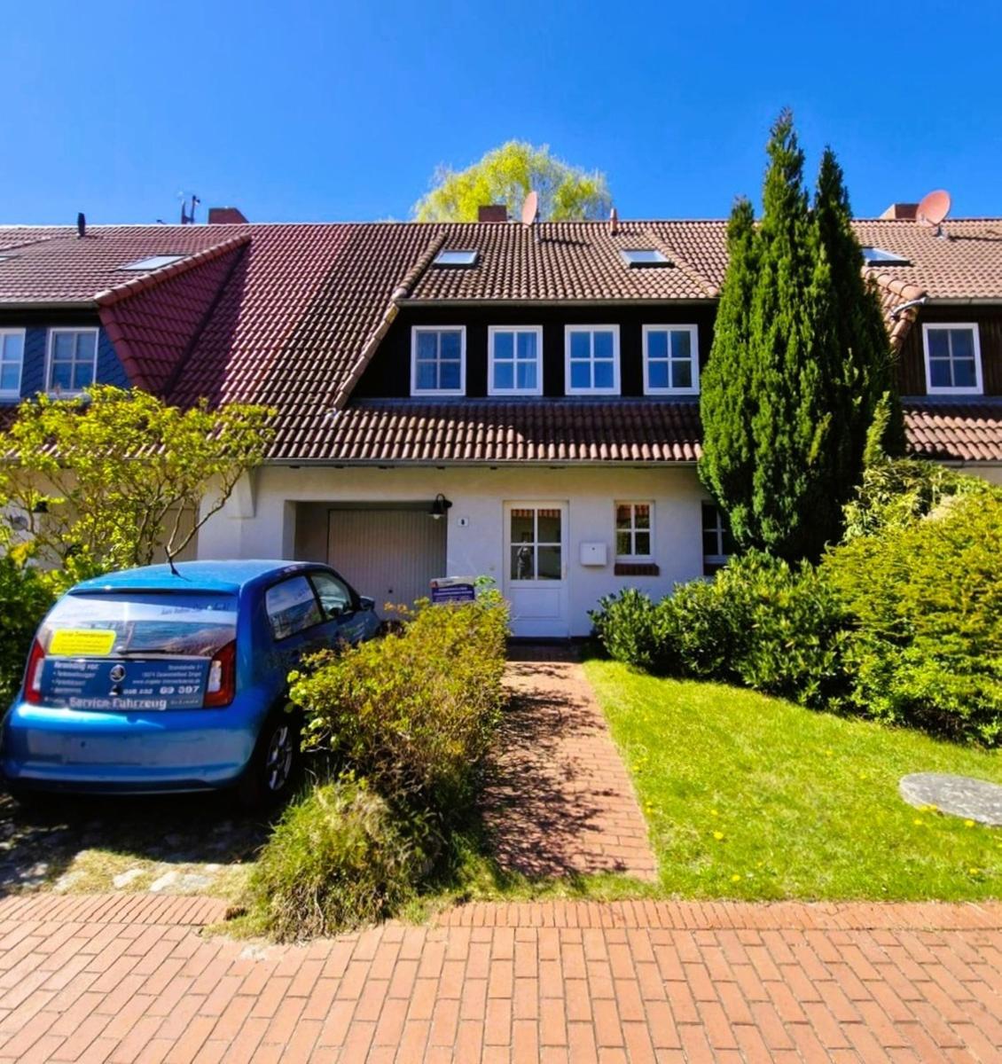 Haus mit rotem Dach, weißen Fenstern und grünem Garten. Vor dem Haus steht ein blauer Wagen.