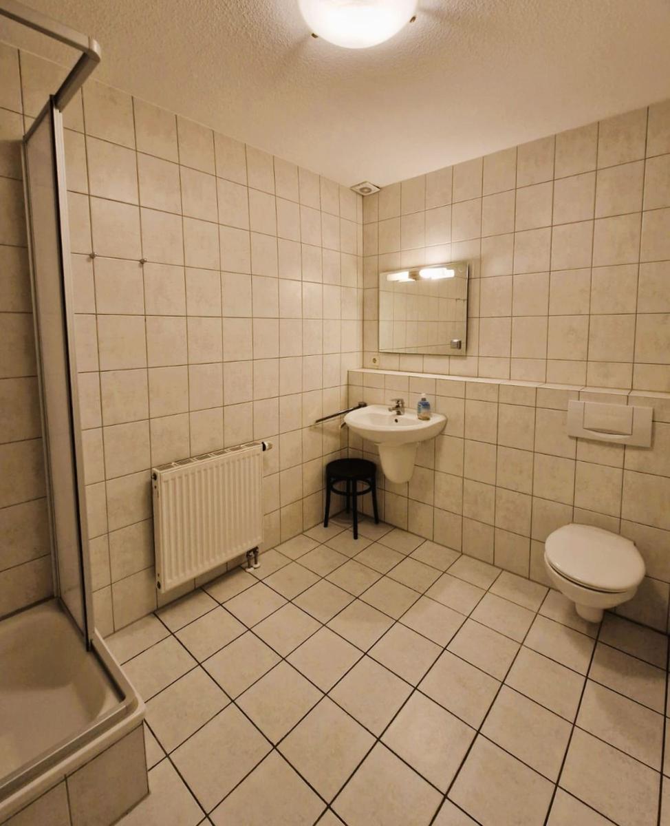 Badezimmer mit Dusche, Waschbecken und Toilette. Fliesenwand und Boden.