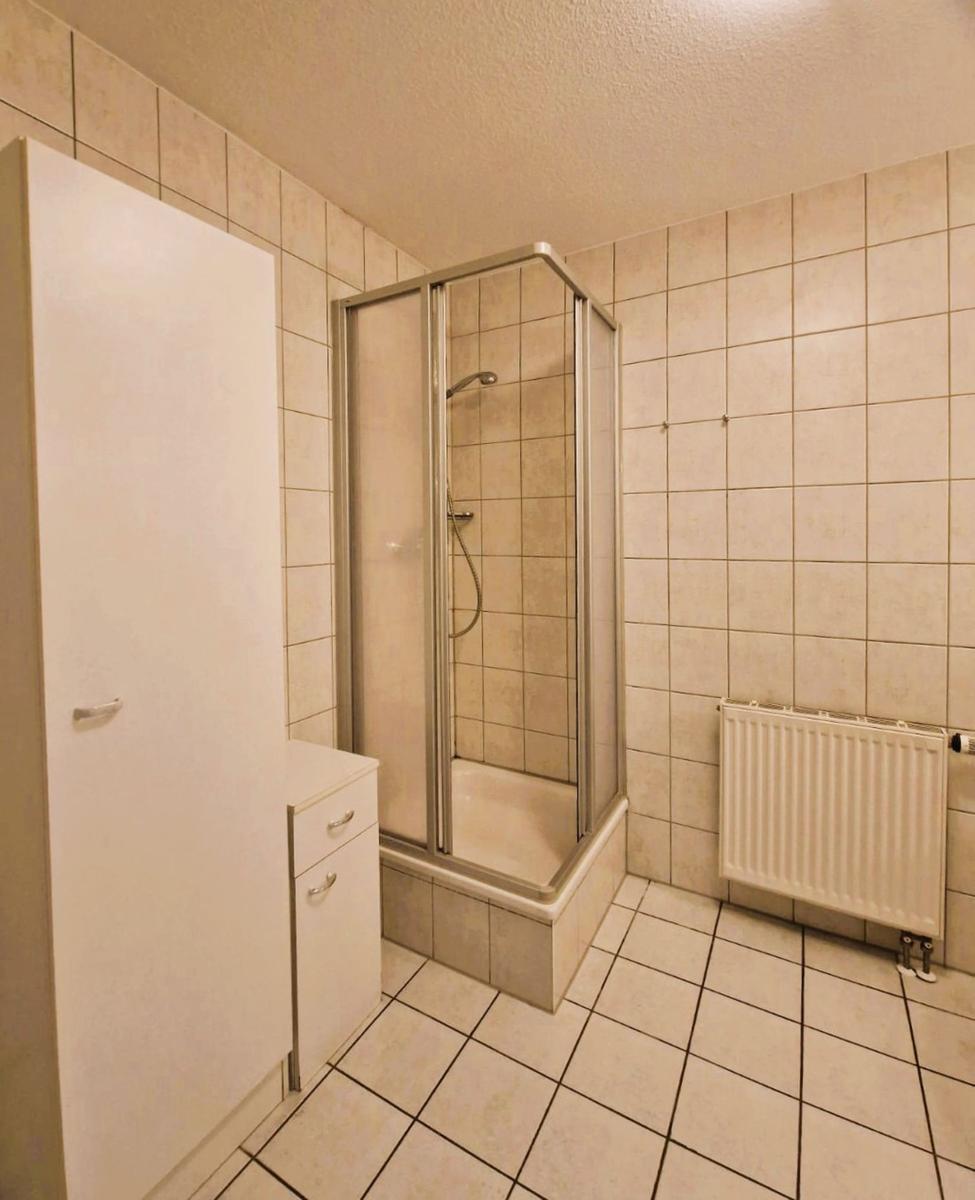 Badezimmer mit Dusche, Waschbecken und Heizkörper.