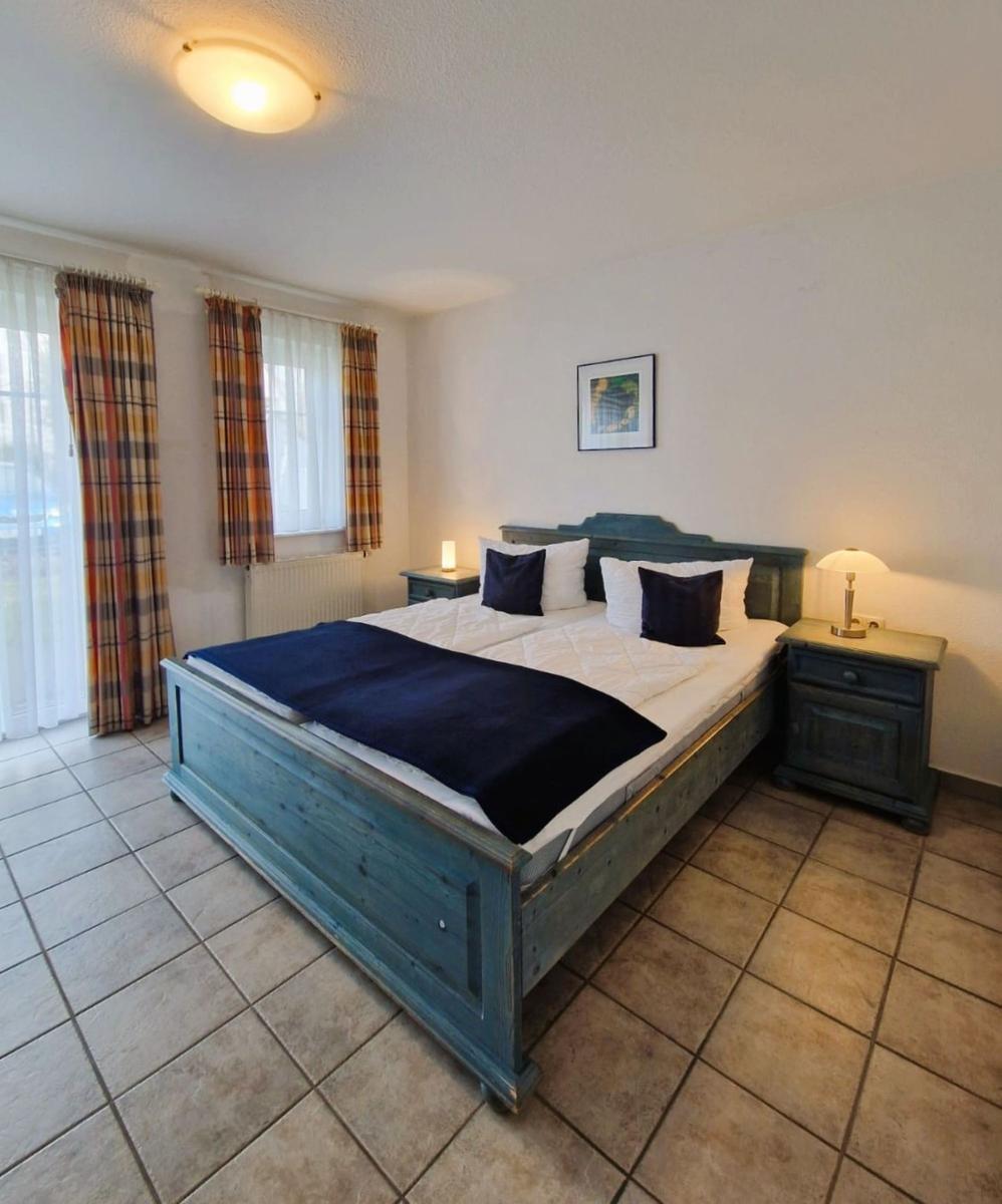 Schlafzimmer mit Bett, Nachttischen und Fenstern mit Vorhängen.